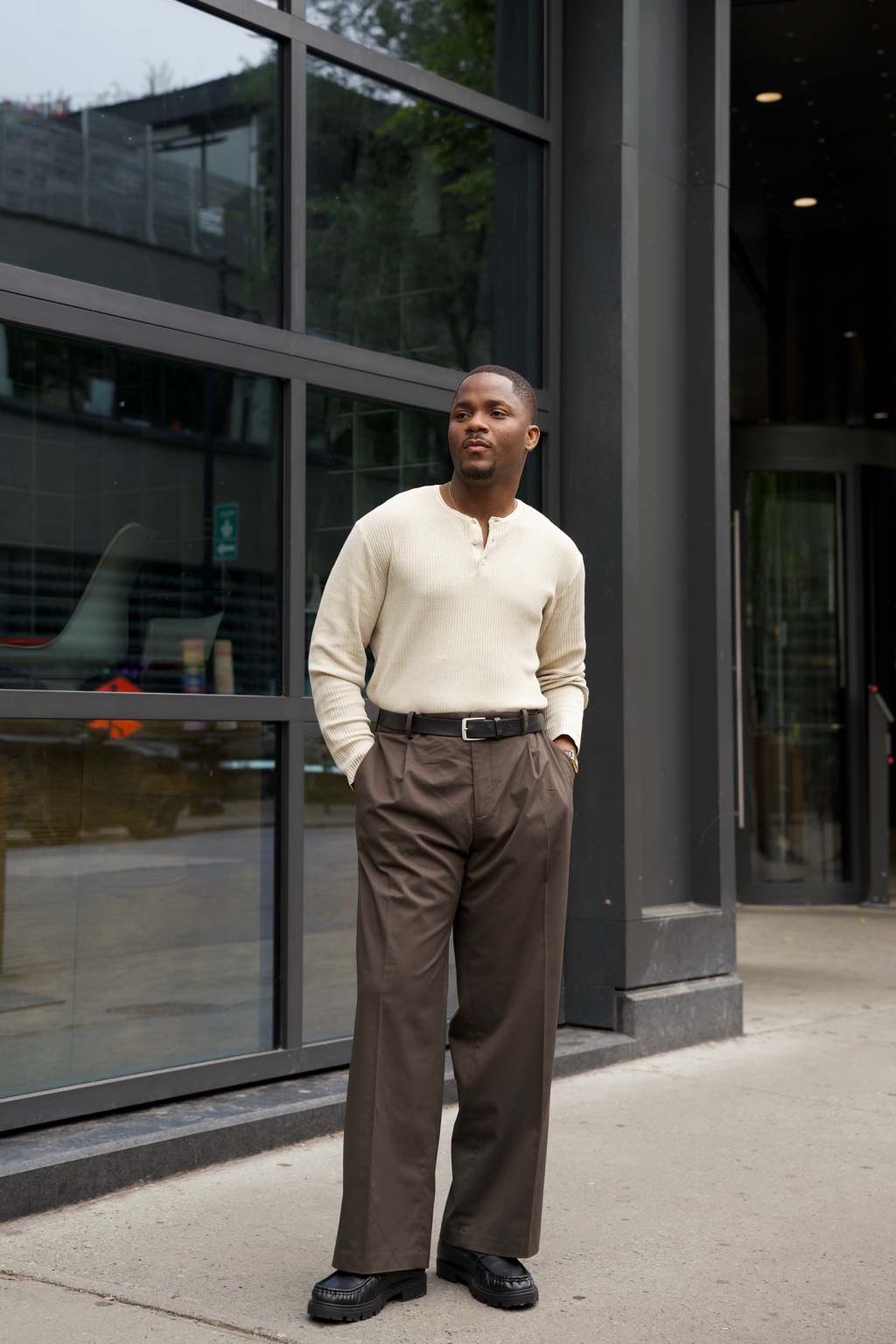 Look masculin élégant TONLAIT : pull crème et pantalon brun devant une façade vitrée